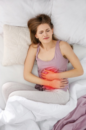 Image of Young woman suffering from abdominal pain in bed, top view