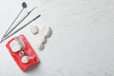 Educational model of gum with post for dental implant between teeth, crowns and medical tools on white wooden background, flat lay