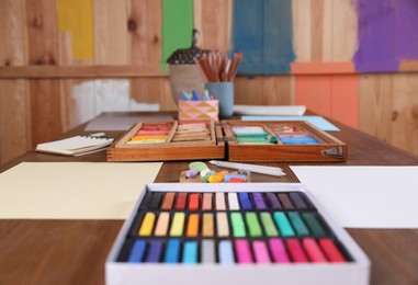 Photo of Blank sheets of paper, colorful chalk pastels and other drawing tools on wooden table indoors. Modern artist's workplace