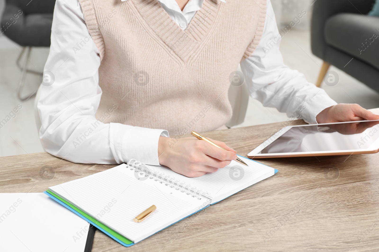 Photo of Woman taking notes while using tablet at wooden table in office, closeup