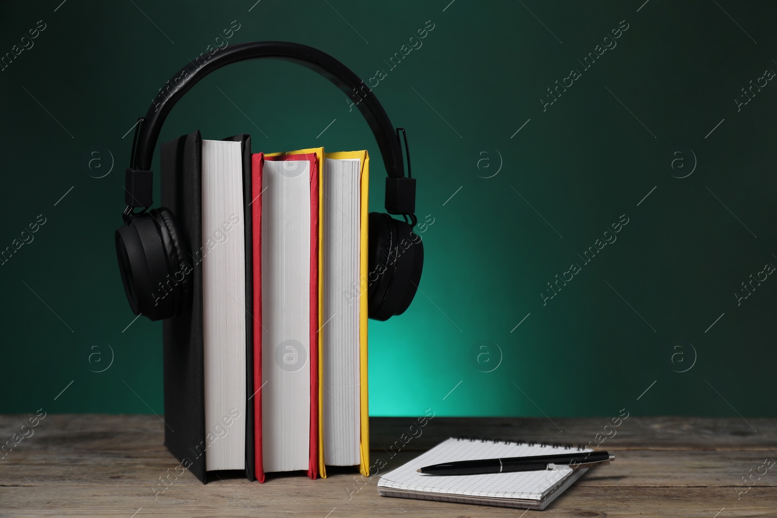 Photo of Learning foreign language. Flag of Germany made of books, headphones, notebook and pen on wooden table against dark green background, space for text