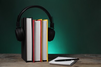 Photo of Learning foreign language. Flag of Germany made of books, headphones, notebook and pen on wooden table against dark green background, space for text