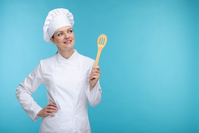 Photo of Happy chef in uniform holding wooden spatula on light blue background, space for text
