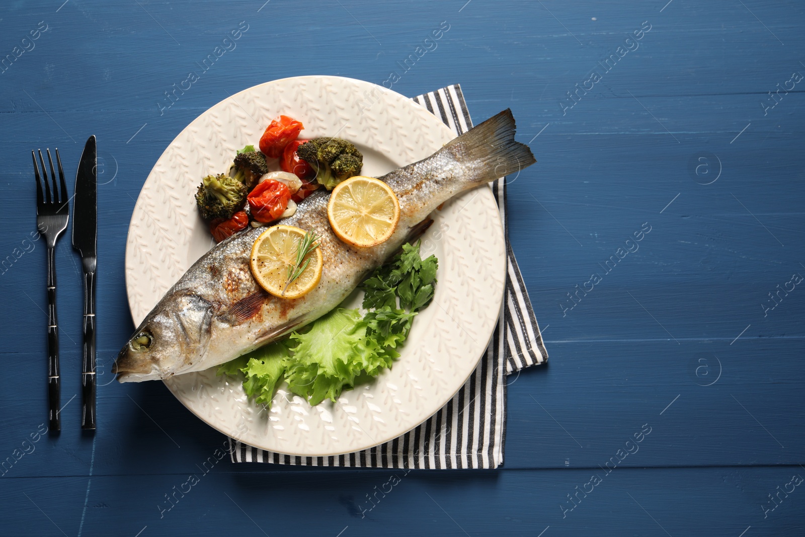 Photo of Delicious baked fish and vegetables served on blue wooden table, top view. Space for text