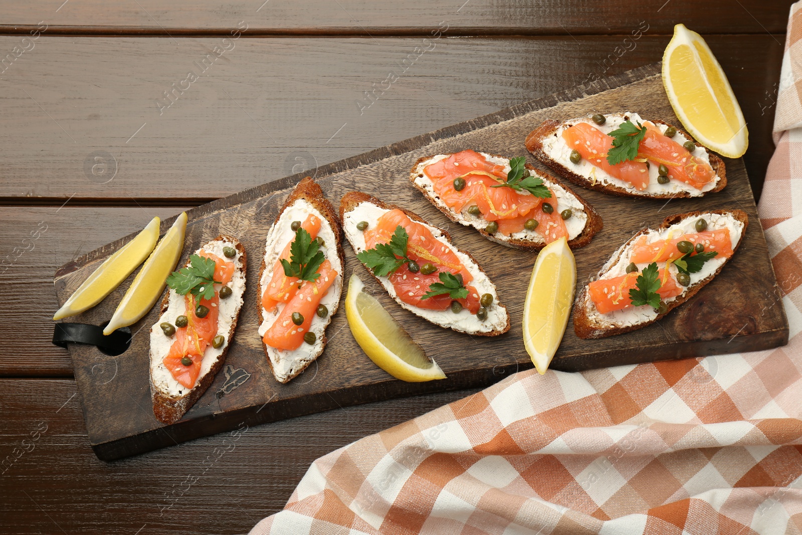 Photo of Tasty canapes with salmon, capers, lemon and cream cheese on wooden table, top view