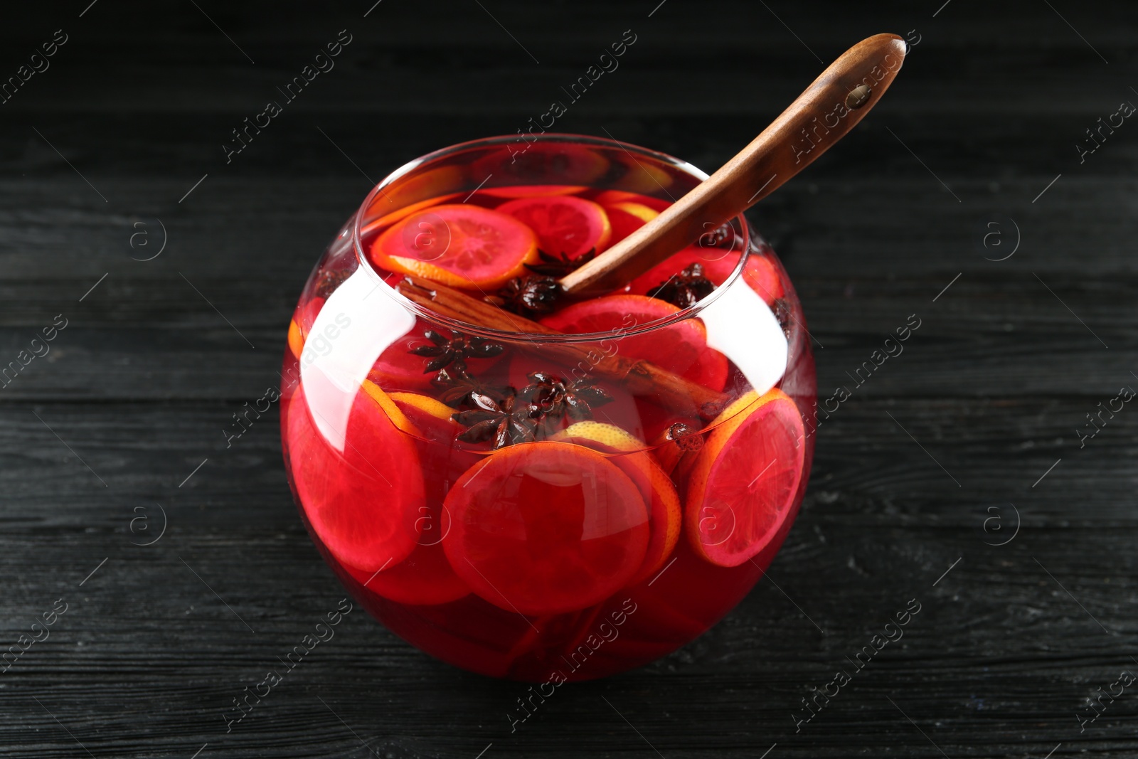 Photo of Glass bowl of delicious aromatic punch drink and ladle on black wooden table