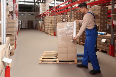 Photo of Worker wrapping boxes in stretch film at warehouse