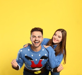 Couple wearing Christmas sweaters on yellow background