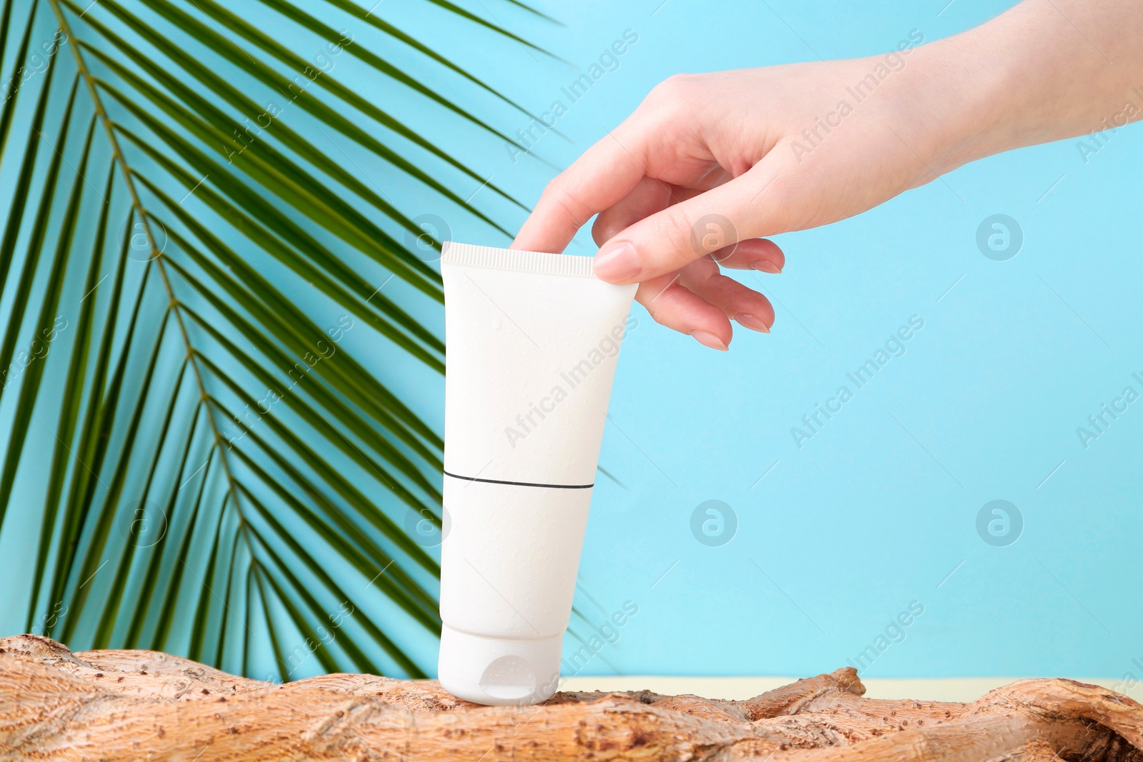 Photo of Woman with tube of cream and plant against light blue background, closeup