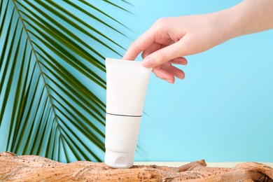 Woman with tube of cream and plant against light blue background, closeup