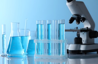 Photo of Microscope near different laboratory glassware and test tubes with light blue liquid on table