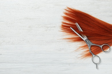 Flat lay composition with red hair, thinning scissors and space for text on white wooden background. Hairdresser service