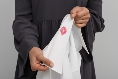 Photo of Woman holding her husband's shirt with lipstick kiss mark against white background, closeup