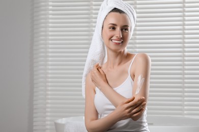 Happy woman applying body cream onto arm in bathroom, space for text