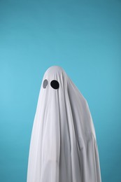 Photo of Creepy ghost. Person covered with white sheet on light blue background