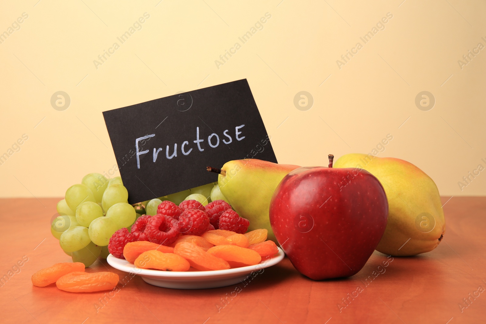 Photo of Card with word Fructose, delicious ripe fruits, raspberries and dried apricots on wooden table