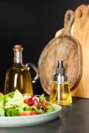 Plate of salad and bottles with cooking oil on black table in kitchen