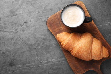 Tasty fresh croissant and coffee on grey table, top view. Space for text