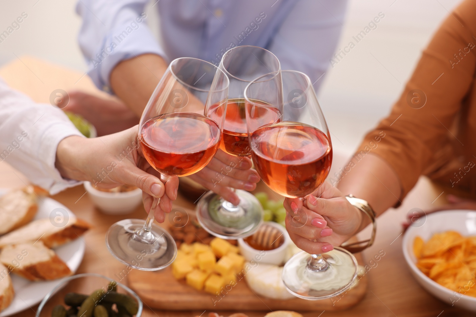 Photo of People clinking glasses with rose wine above wooden table indoors, closeup