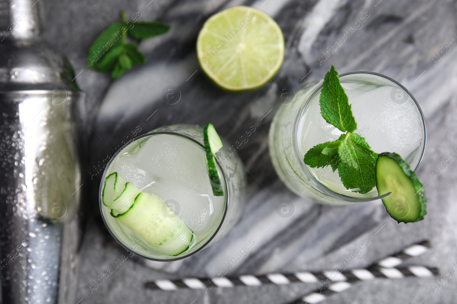 Photo of Glasses of refreshing cucumber water with ice grey on table, flat lay