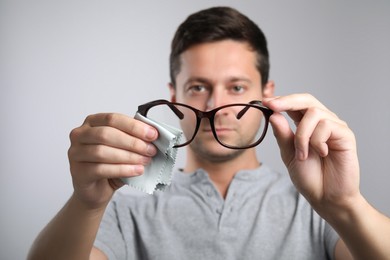 Photo of Man wiping glasses with microfiber cloth on light grey background, selective focus