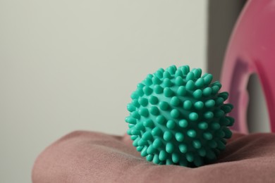 Photo of Turquoise dryer ball on brown soft clothing, closeup