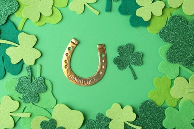 St. Patrick's day. Golden horseshoe and decorative clover leaves on green background, flat lay