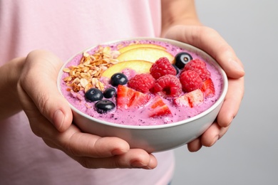 Woman holding bowl with tasty acai smoothie and fruits on light grey background, closeup