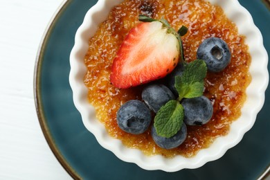 Photo of Delicious creme brulee with berries and mint in bowl on white table, top view