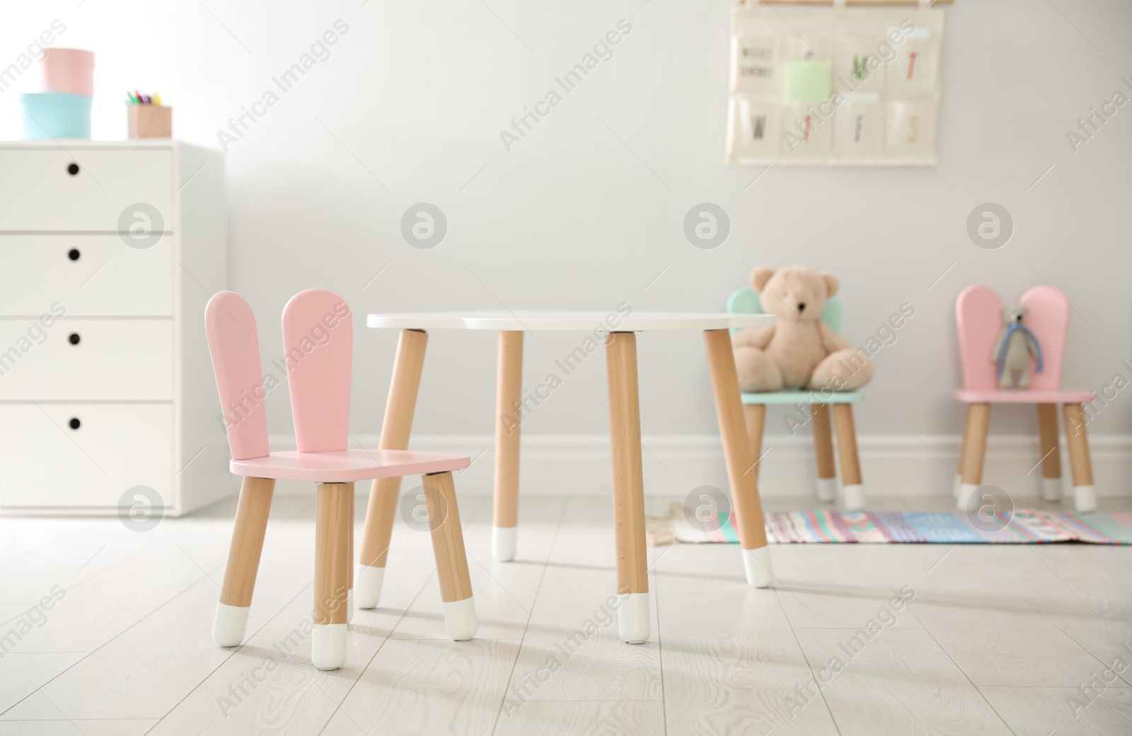 Photo of Small table and pink chair with bunny ears indoors. Children's room interior