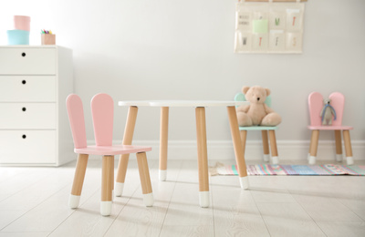 Small table and pink chair with bunny ears indoors. Children's room interior