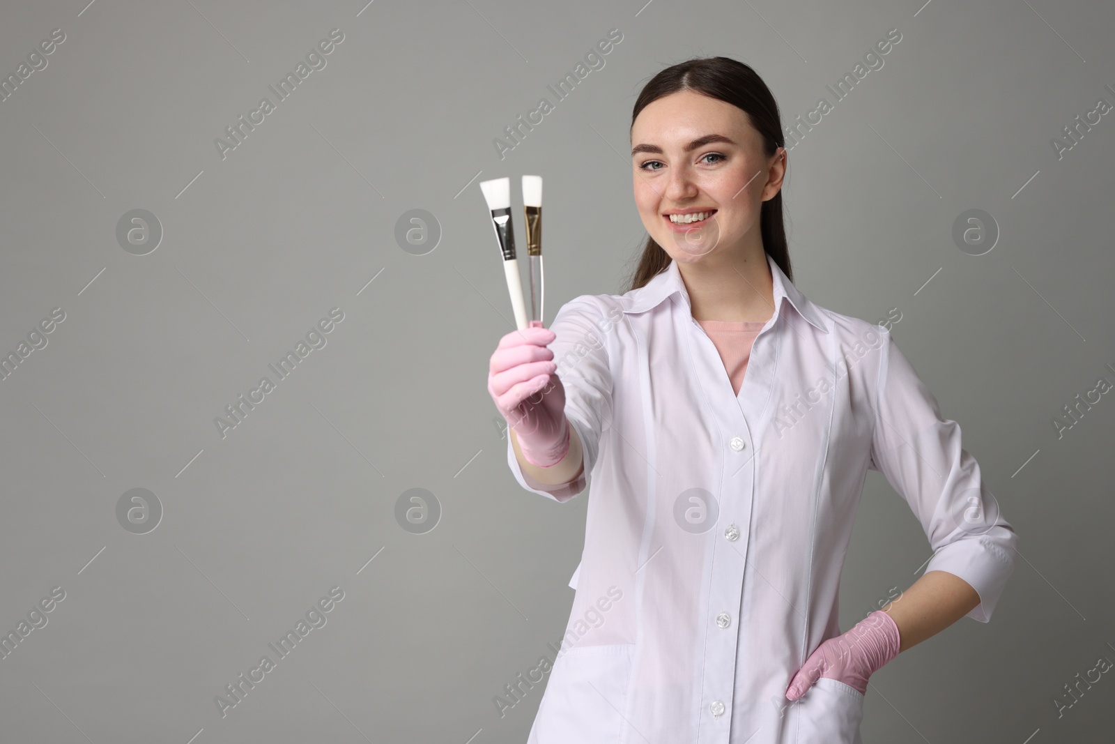 Photo of Cosmetologist with cosmetic brushes on grey background, space for text