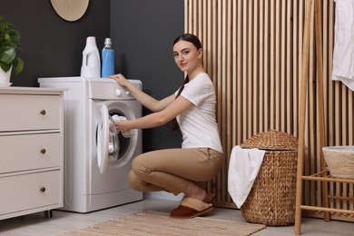 Photo of Beautiful woman putting shirt into washing machine in laundry room