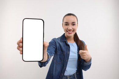 Young woman showing smartphone in hand and pointing at it on white background