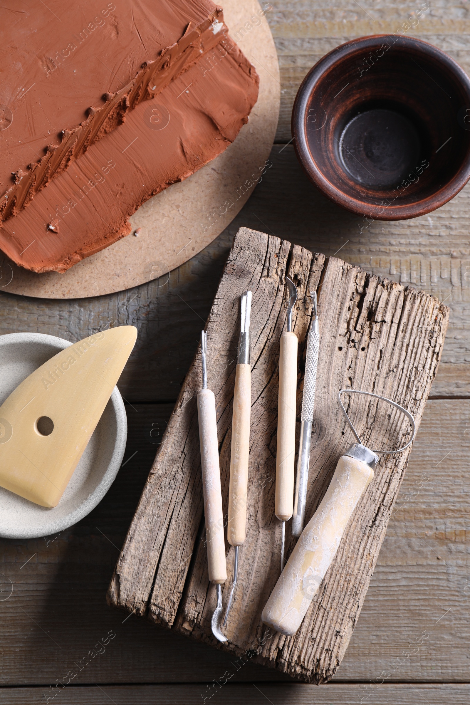 Photo of Clay and set of modeling tools on wooden table, flat lay