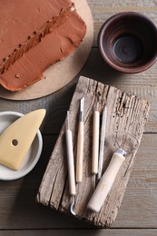 Photo of Clay and set of modeling tools on wooden table, flat lay