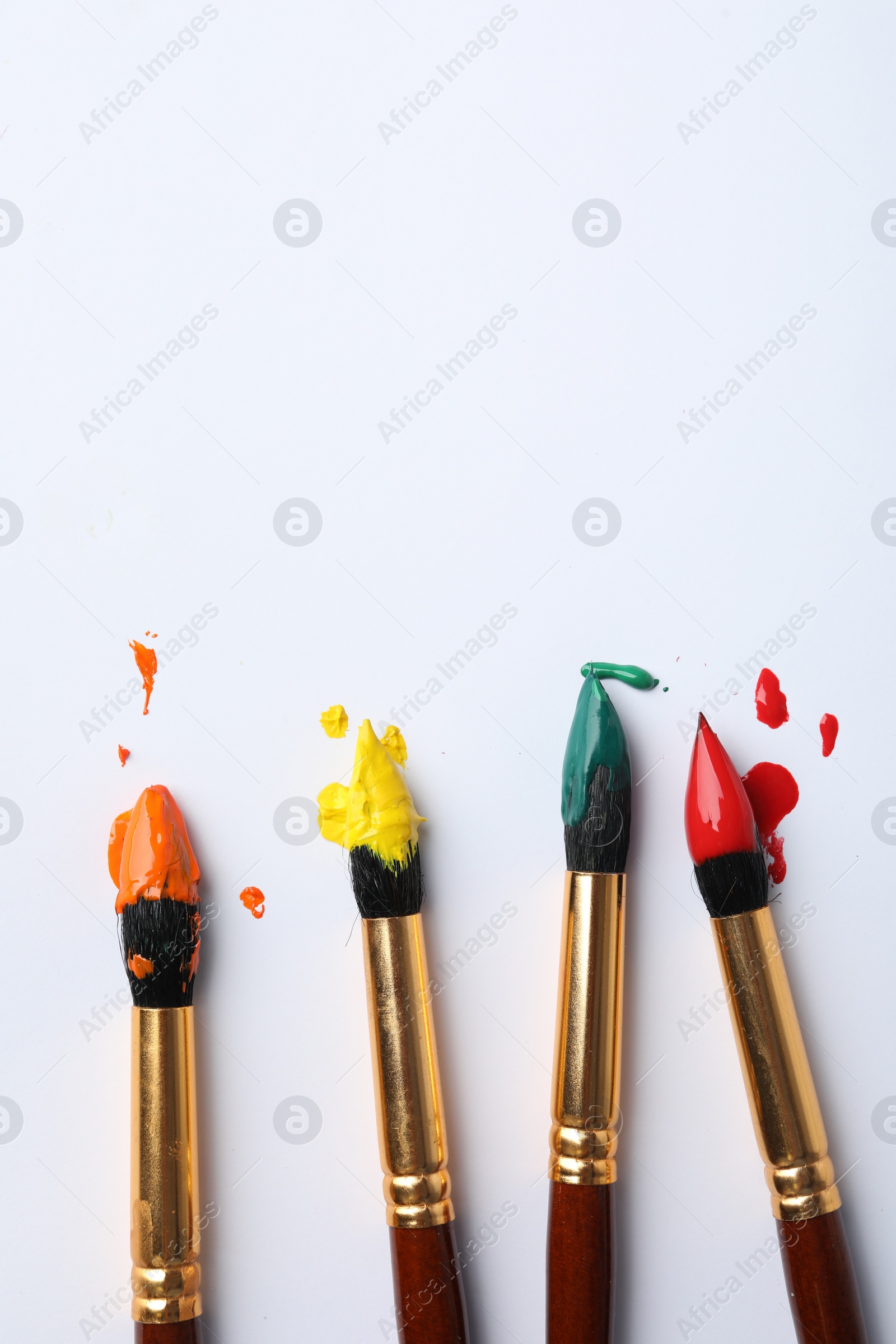 Photo of Brushes with colorful paints on white background, flat lay. Space for text