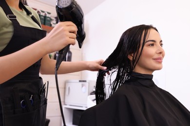 Hairdresser drying woman's hair in beauty salon, closeup