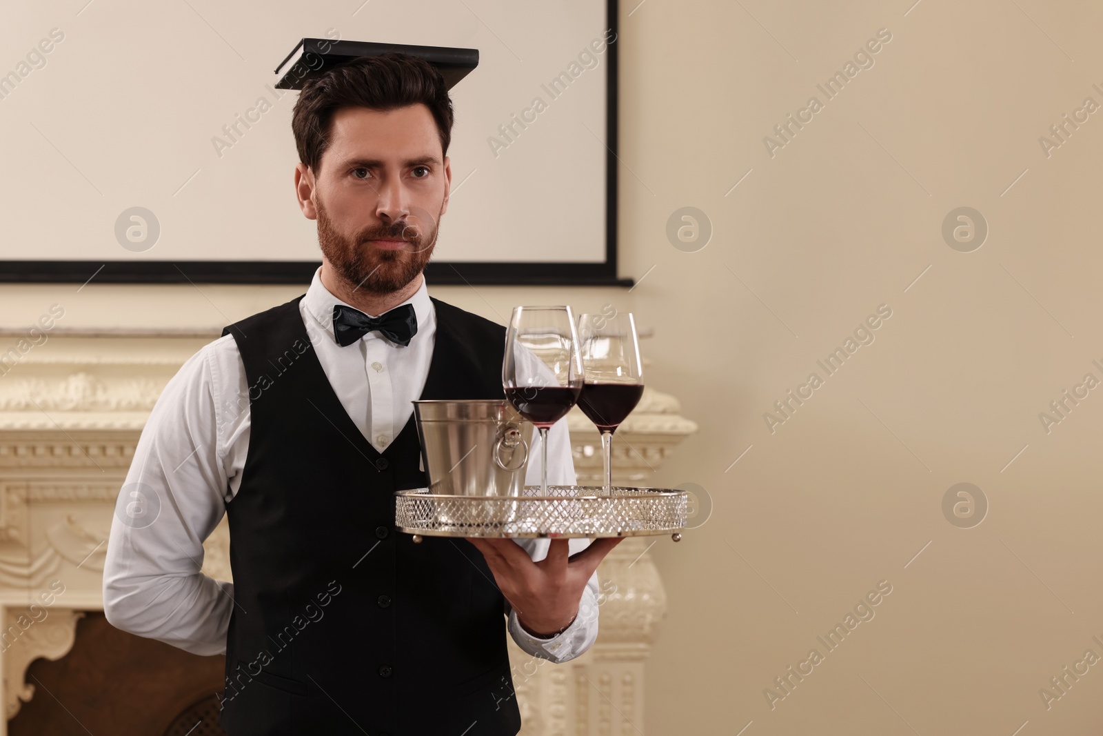 Photo of Man with tray and book on head practicing good posture indoors, space for text. Professional butler courses