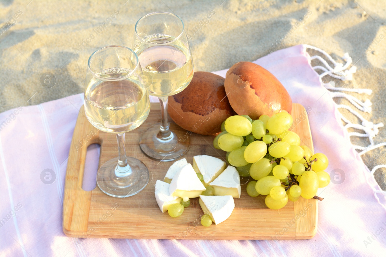 Photo of Glasses with white wine and snacks for beach picnic on sand outdoors