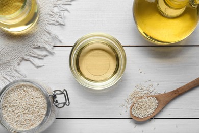 Jar of organic sesame oil and seeds on white wooden table, flat lay