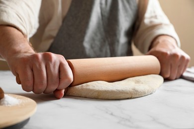 Man rolling raw dough at white table, closeup