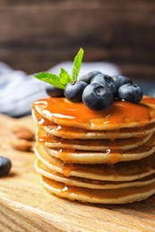 Photo of Wooden board with pancakes, syrup and blueberries on table, closeup