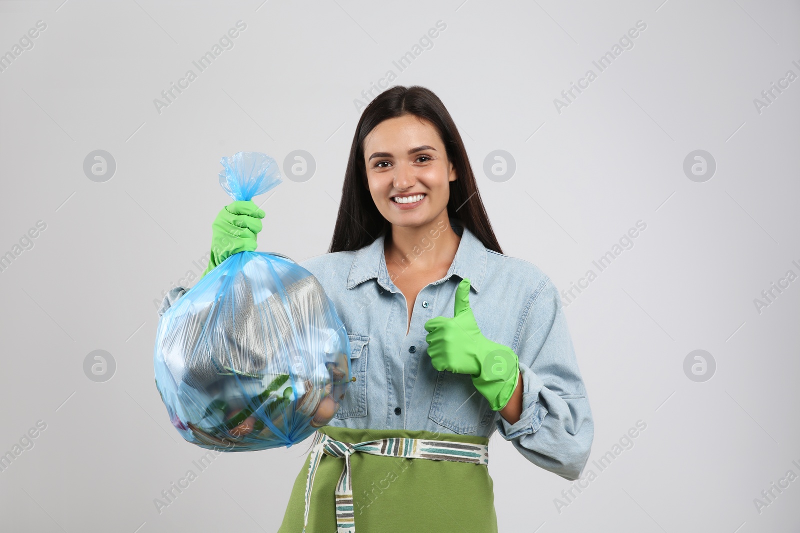 Photo of Woman holding full garbage bag on light background