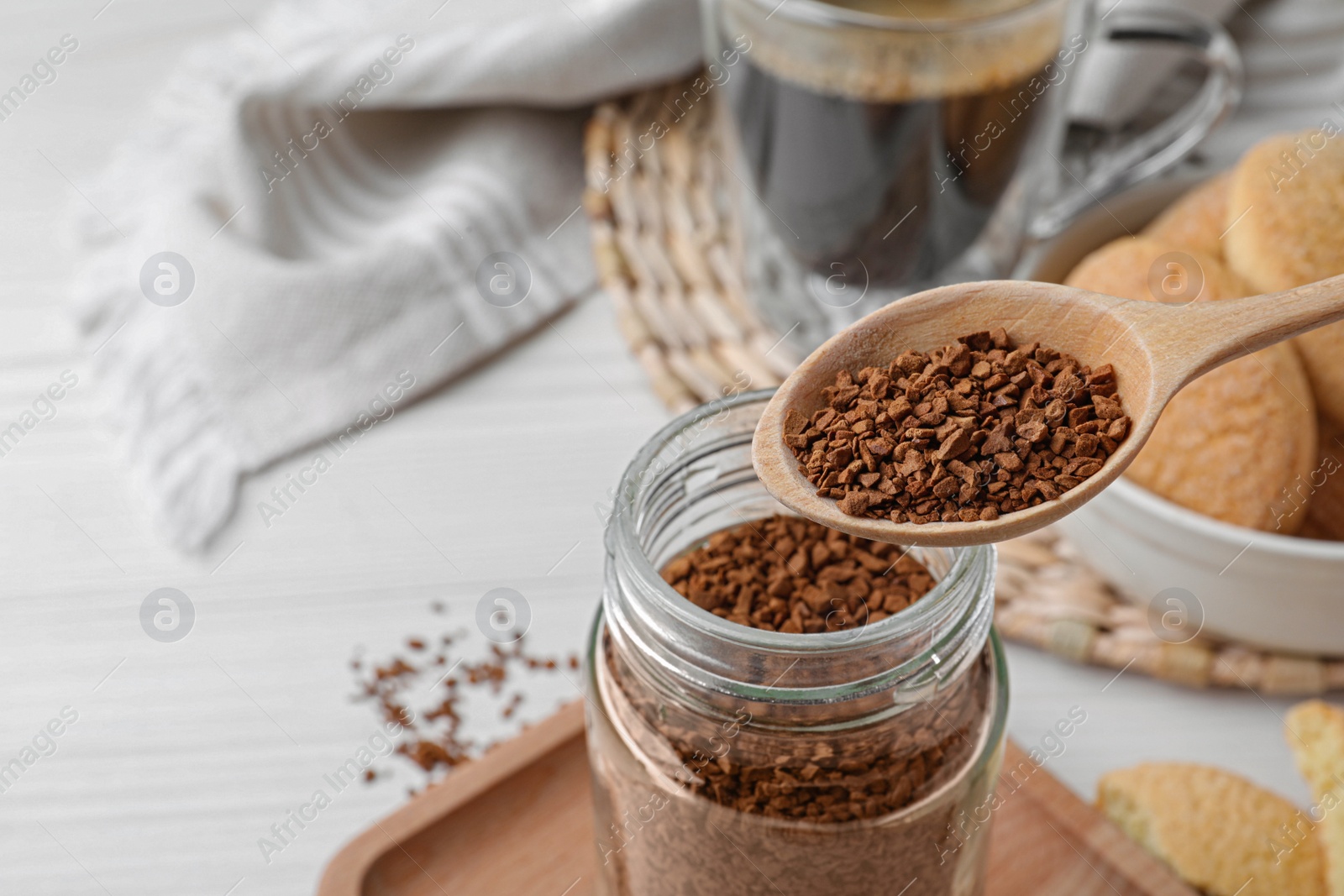 Photo of Spoon of instant coffee over jar on white table, closeup. Space for text