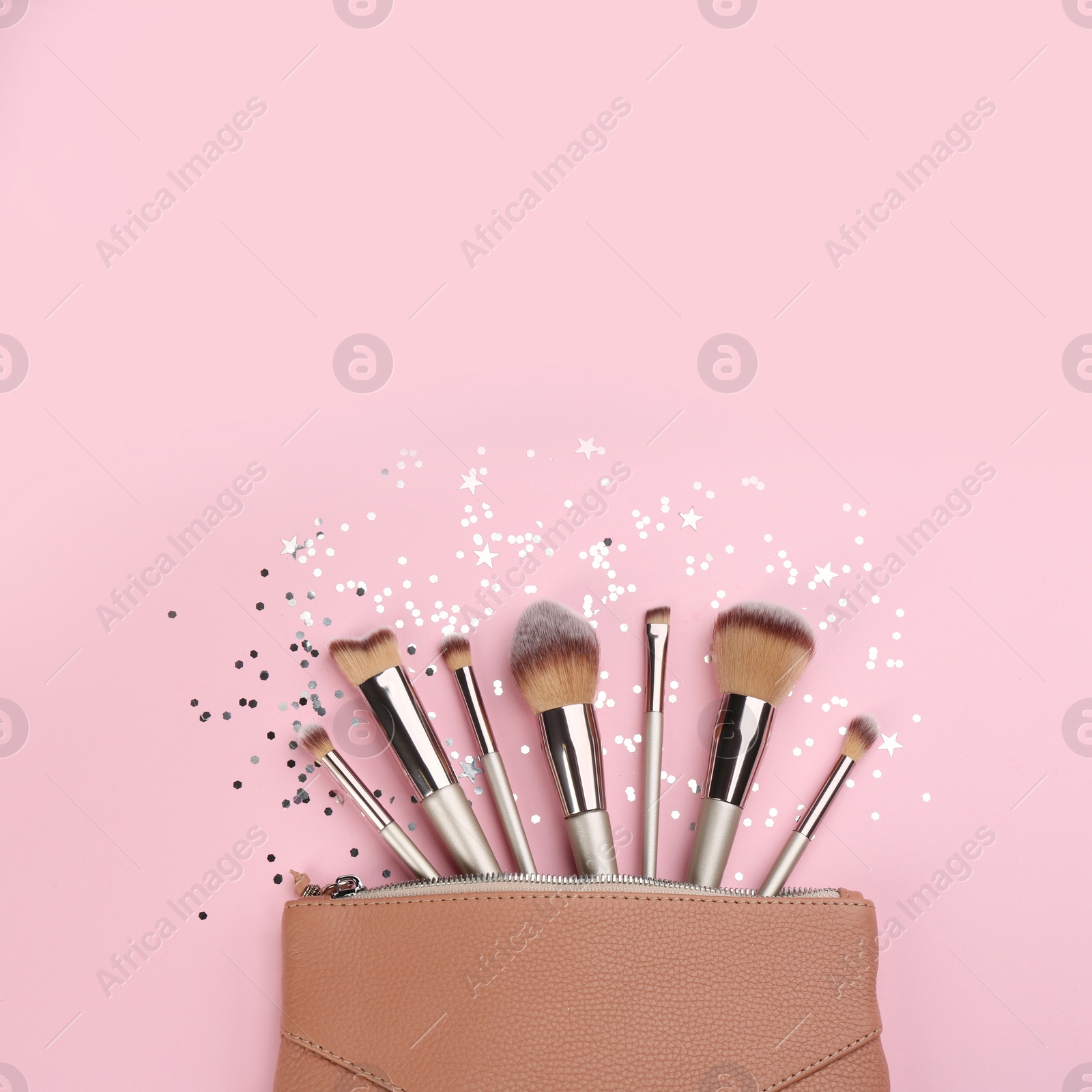 Photo of Different makeup brushes, case and shiny confetti on pink background, flat lay