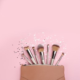 Different makeup brushes, case and shiny confetti on pink background, flat lay