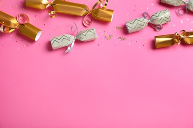 Photo of Open and closed Christmas crackers with shiny confetti on pink background, flat lay. Space for text