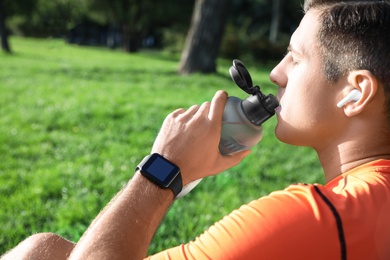 Photo of Man with fitness tracker drinking water after training in park, closeup