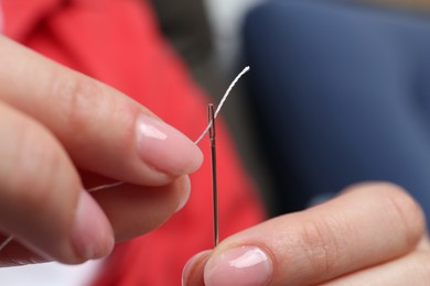 Woman inserting thread through eye of needle on blurred background, closeup